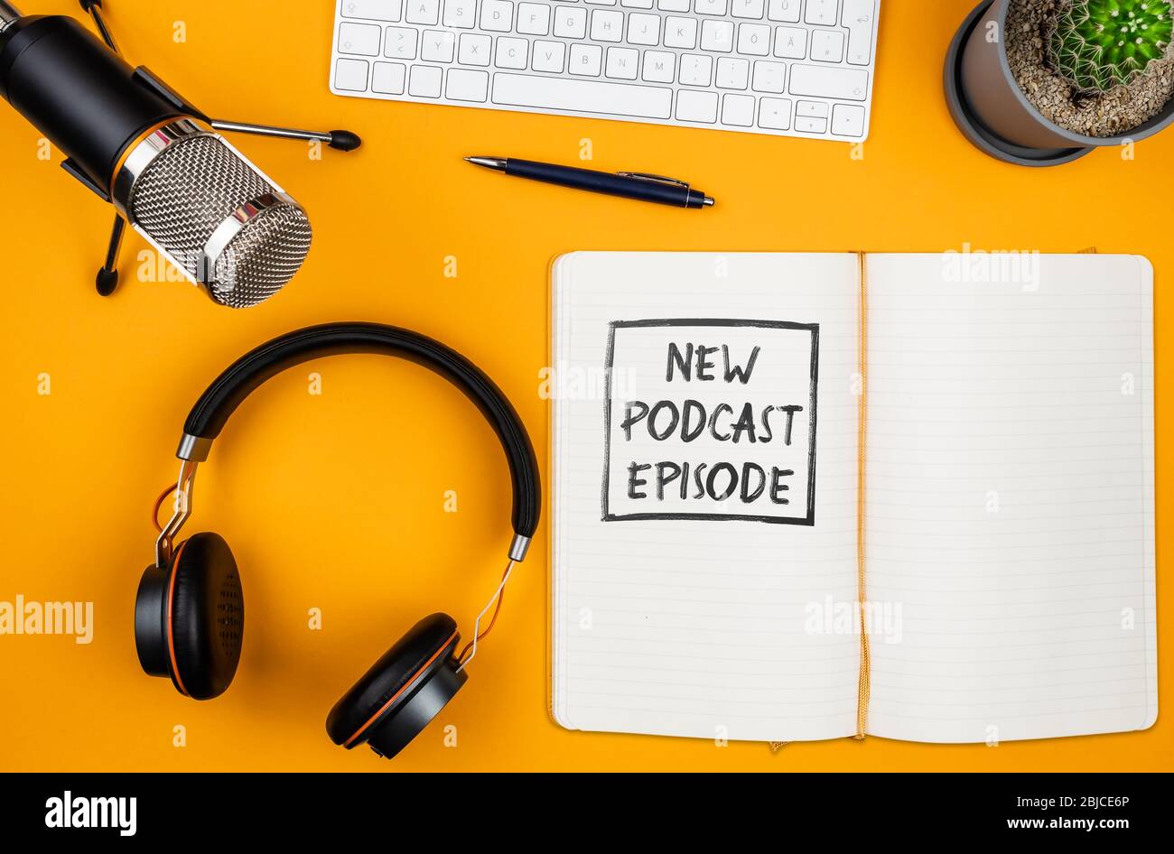 top view of text NEW PODCAST EPISODE on notepad on desk with microphone, computer keyboard and headphones, podcasting concept Stock Photo