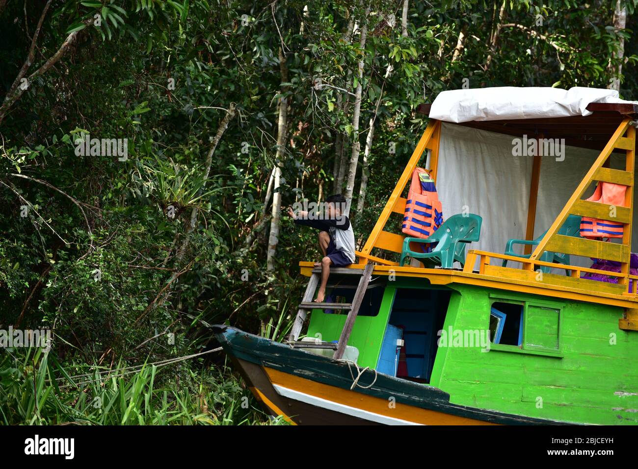 Indonesian boy in a boat with a slingshot in the jungle of Kalimantan. Stock Photo
