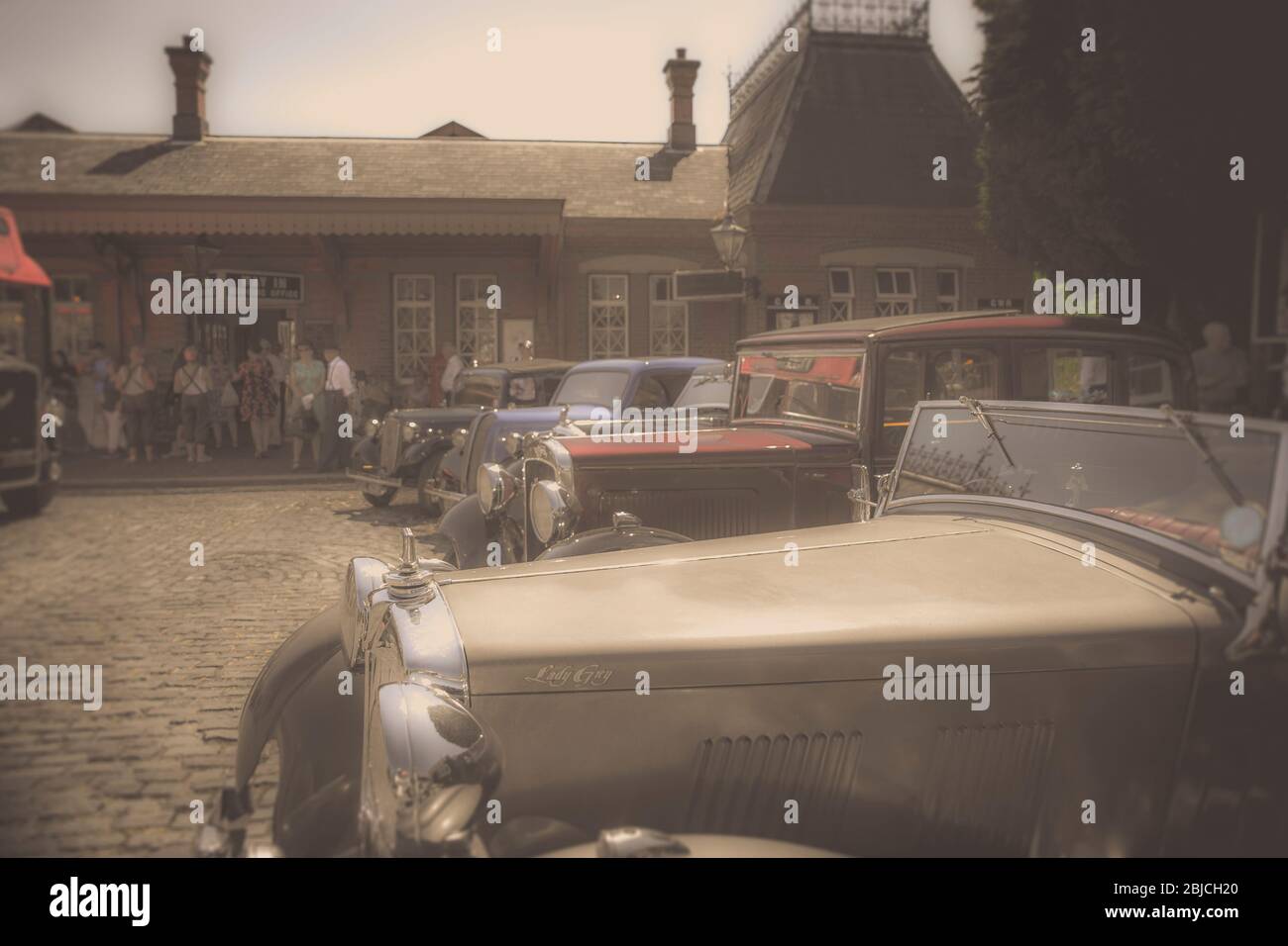 Nostalgic dreamlike view of vintage, classic cars parked outside heritage railway station, 1940s WWII wartime summer event UK. Vintage car. Nostalgia. Stock Photo