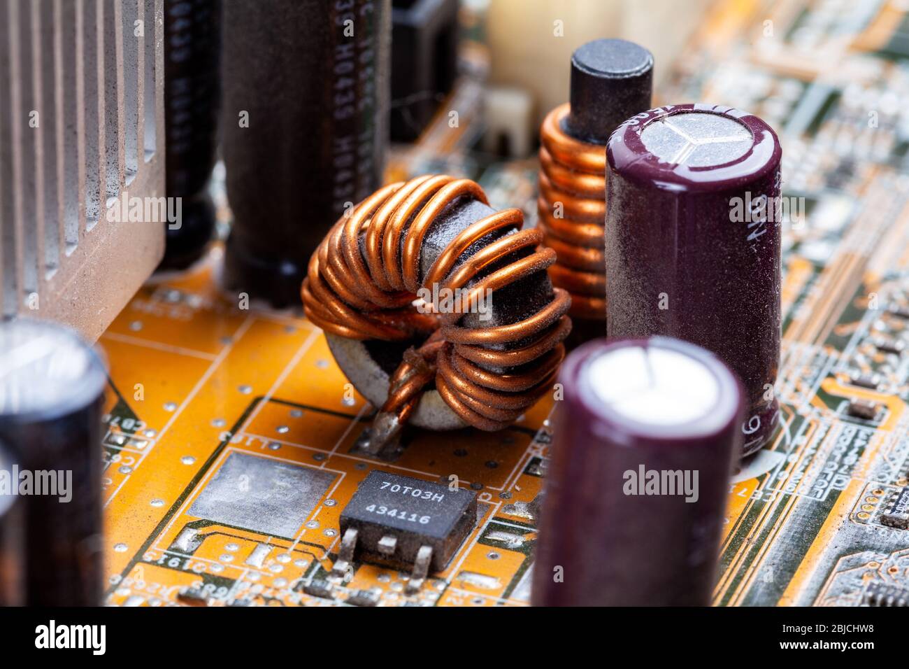 Copper coil, inductor winding part on a pc motherboard, circuit board macro, closeup. Coil whine noise issue abstract concept, electronic elements Stock Photo