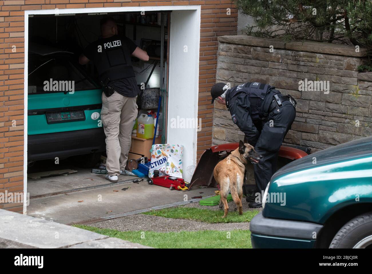 Gelsenkirchen, Germany. 29th Apr, 2020. Police investigators search in a garage of the suspect's house with a tracker dog. A police officer was killed this morning during a SEK operation in Gelsenkirchen. When the officers were about to make a house search on a suspect in a drug investigation, the suspect is said to have fired shots at the SEK officers. One of them hit the SEK policeman. Credit: Bernd Thissen/dpa - ATTENTION: Names on the bell plates were pixelated for legal reasons/dpa/Alamy Live News Stock Photo