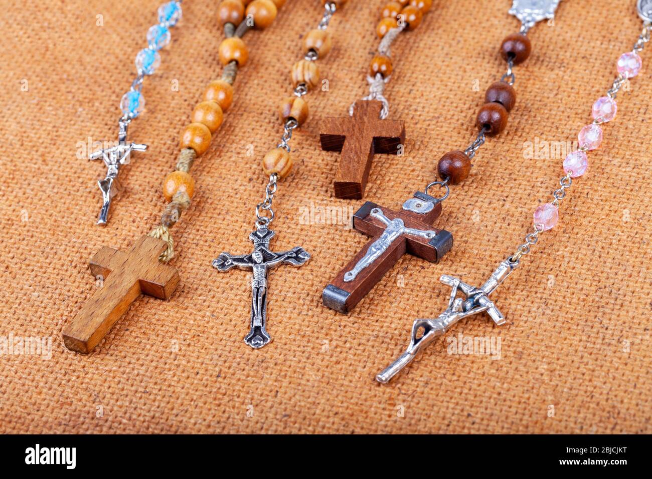 Lots of different styled Christian crosses, multiple rosaries laying on brown background Prayer and belief, christianity symbols abstract concept Stock Photo