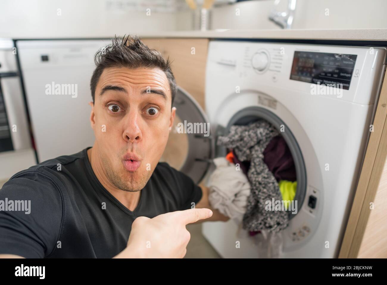 Man putting clothes in the washing machine, in the kitchen, worried because  he has to wash a lot of clothes. Close up Stock Photo - Alamy