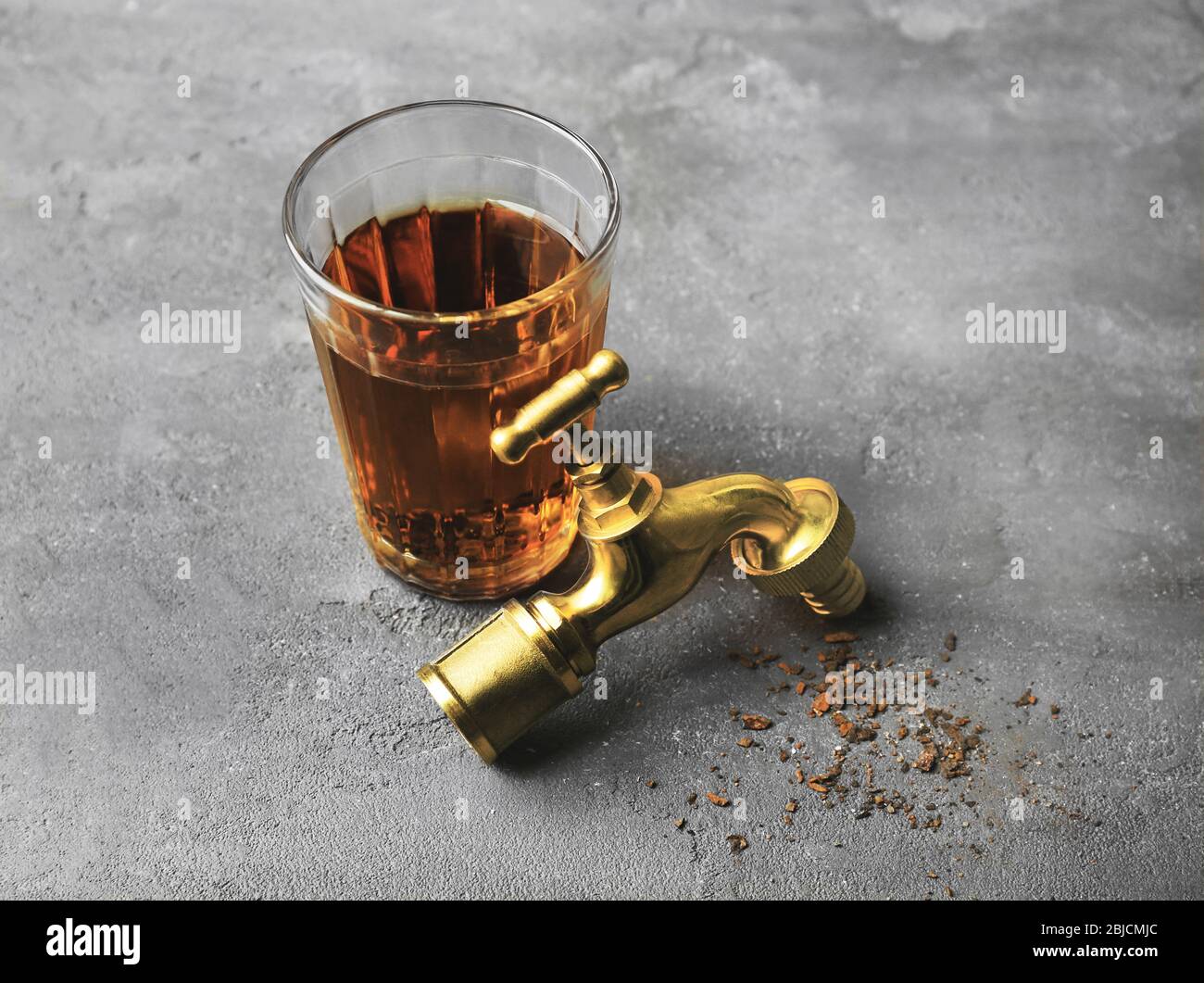 Faucet with glass of dirty water and rust flakes on gray textured ...