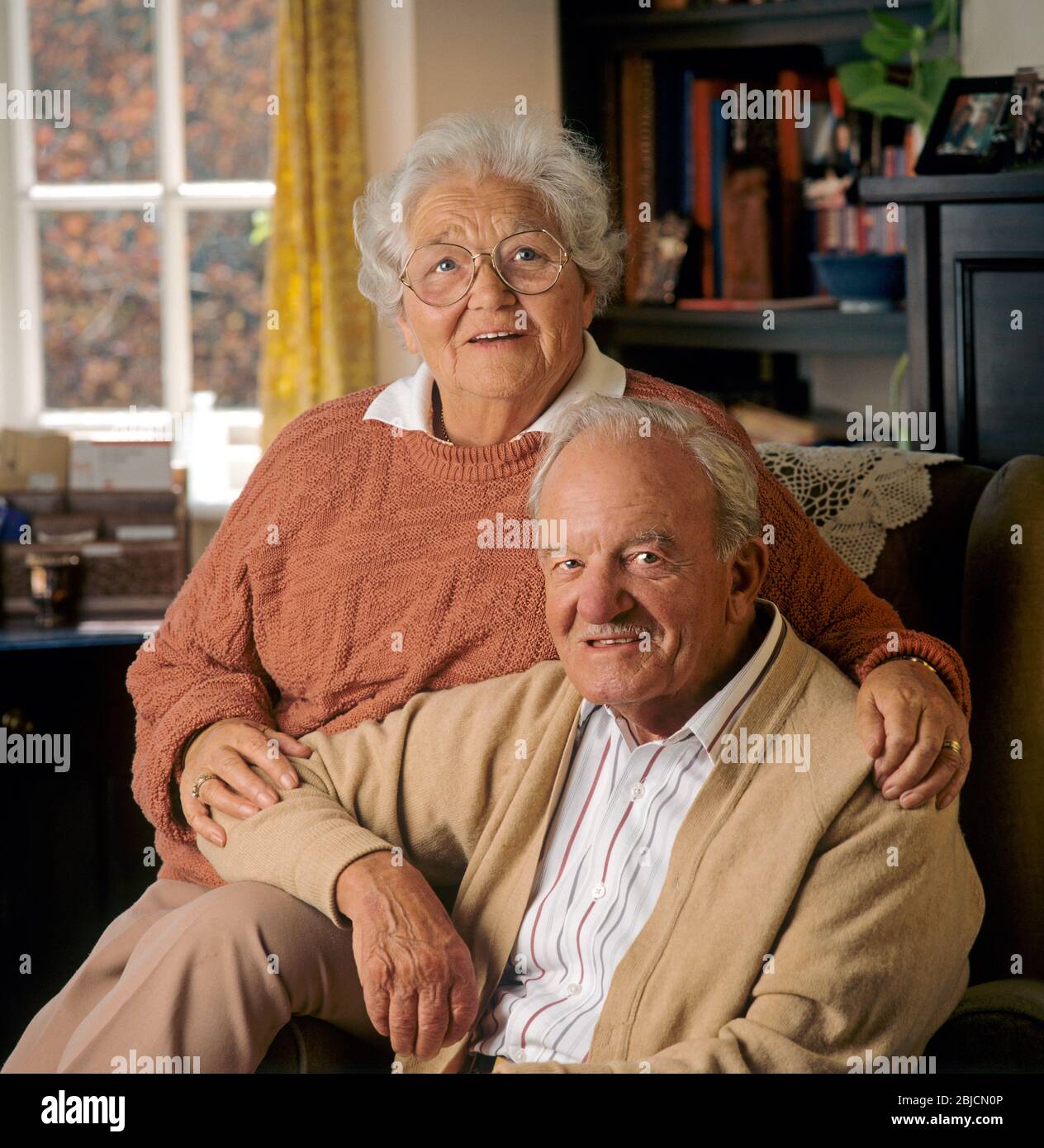 Elderly senior old age pensioner happy couple 80-86 years home owners  sitting in their comfortable living room facing camera Stock Photo