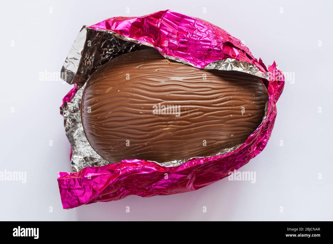 unwrapped Milk chocolate Easter egg in pink silver foil isolated on white background Stock Photo