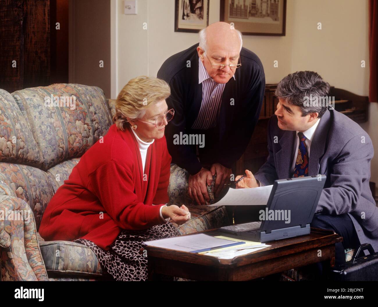 1990s Elderly couple financial review at home, talking to salesman sales person man with IBM ThinkPad laptop & papers. Finance Wills Probate etc Stock Photo