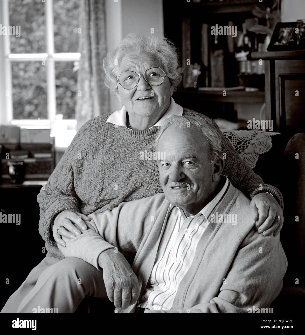 Elderly senior old age pensioner happy couple 80-86 years home owners  sitting in their comfortable living room facing camera B&W Stock Photo