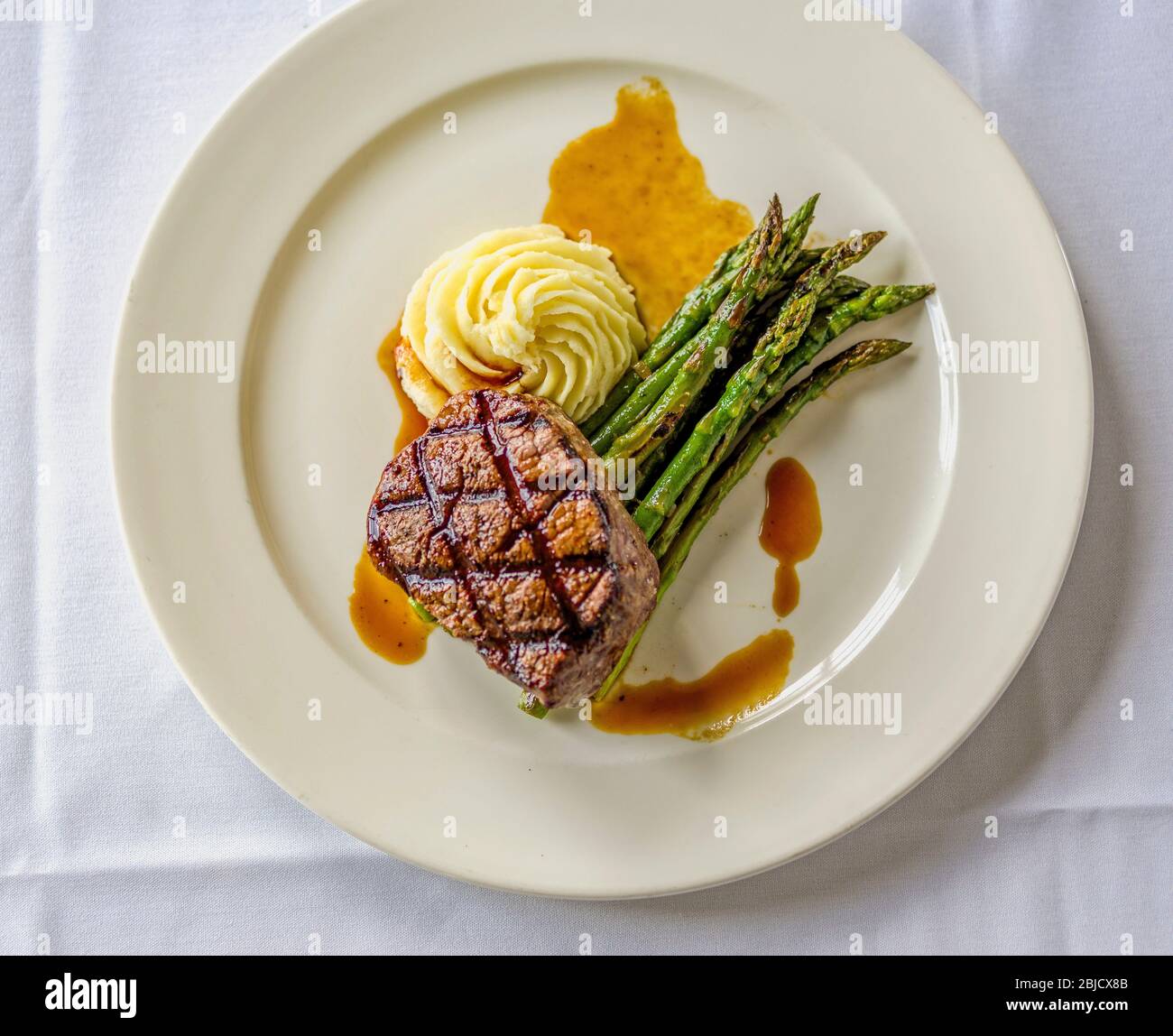 Grilled ribeye steak with creamy potatoes, grilled asparagus, au jus sauce, on white plate Stock