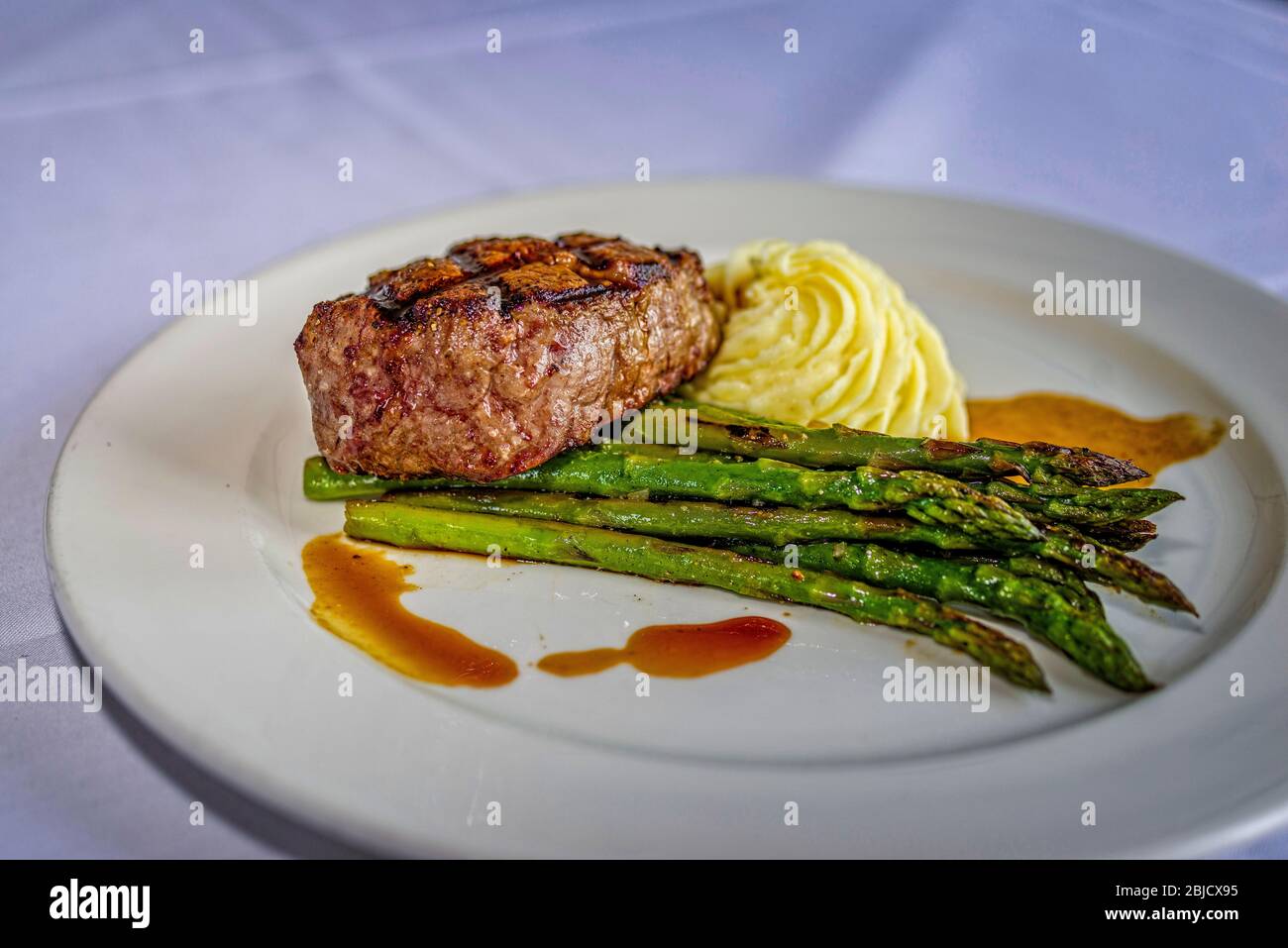 Grilled ribeye steak with creamy potatoes, grilled asparagus, au jus sauce, on white plate Stock