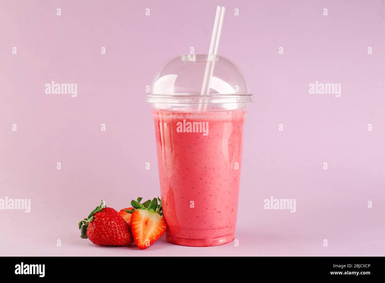 Delicious strawberry milkshake in plastic cup on pink background Stock Photo
