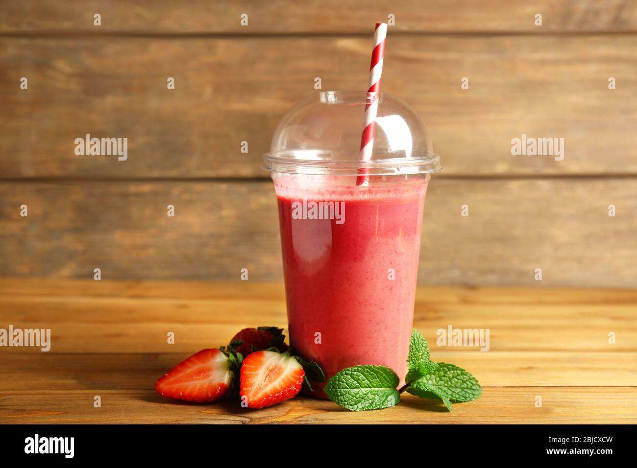 Delicious strawberry milkshake in plastic cup on wooden background Stock Photo