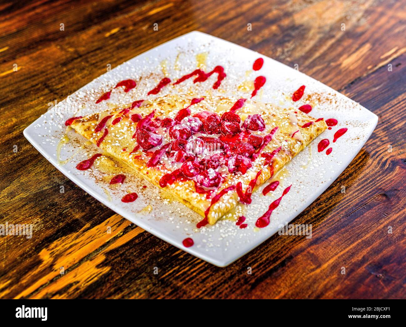 Triangle shaped, dessert crepe with raspberry sauce on white plate ...