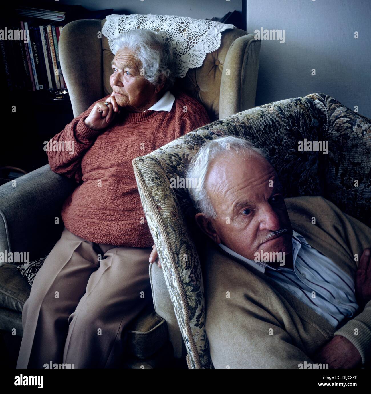 Elderly senior old age couple at home together with pensive thoughtful expressions sitting facing away from each other Stock Photo