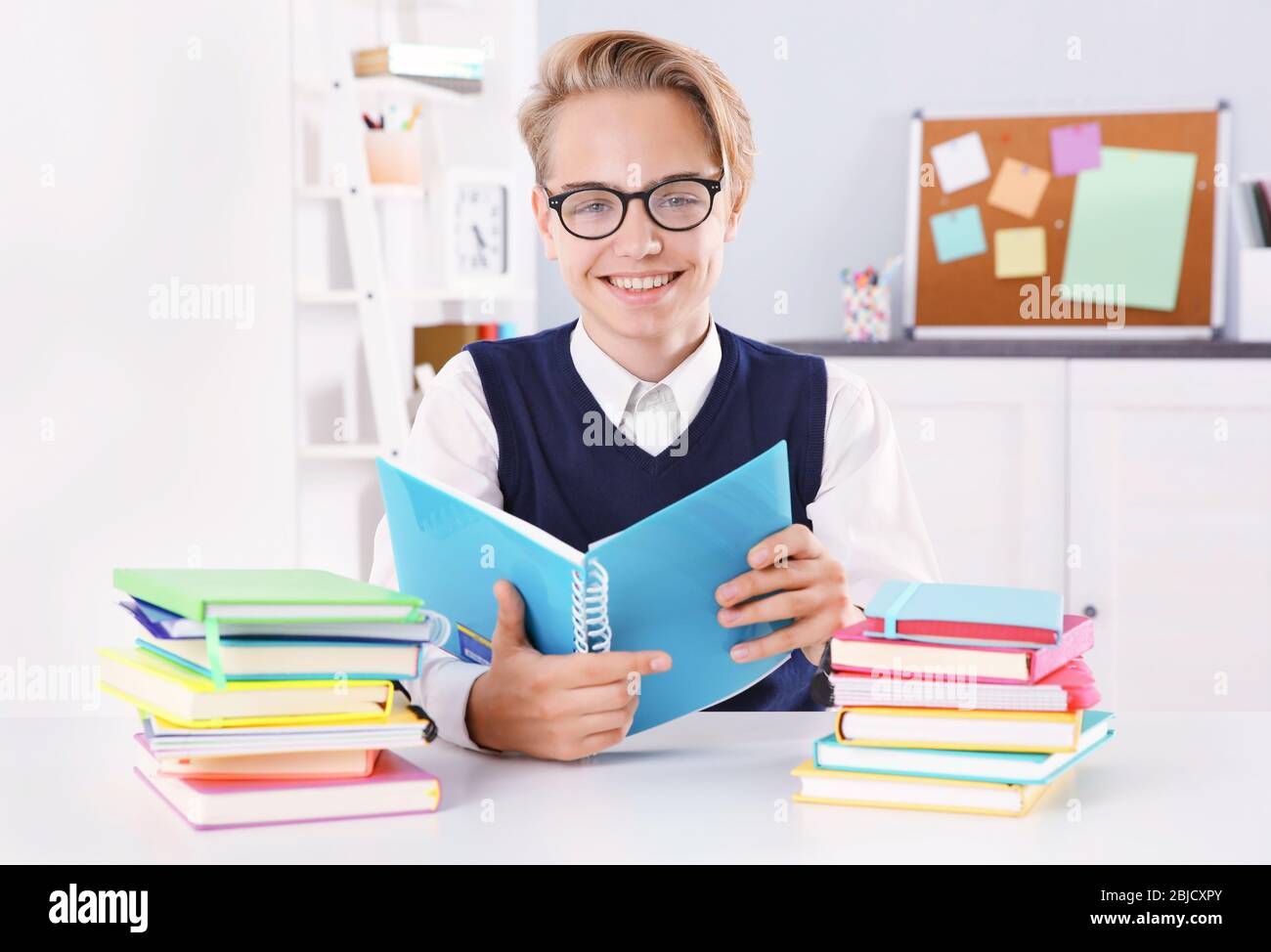 Pupil with pile of books sitting at desk in a classroom Stock Photo - Alamy