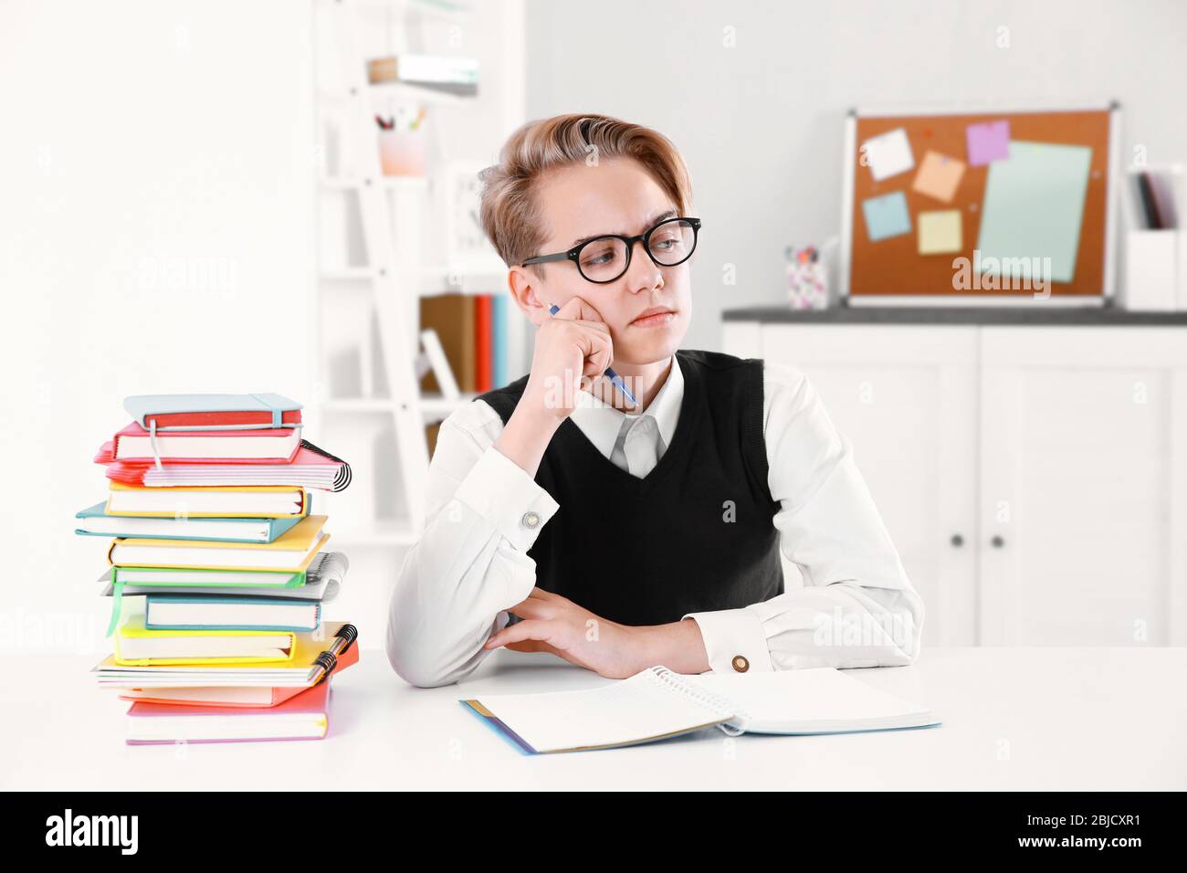 Pupil with pile of books sitting at desk in a classroom Stock Photo - Alamy