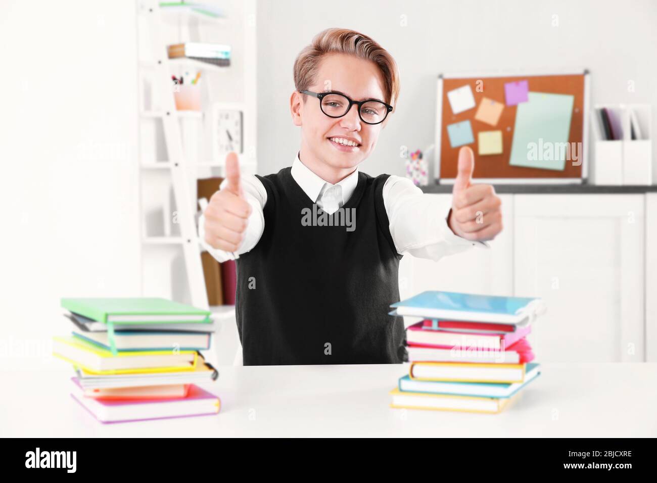 Pupil with pile of books sitting at desk in a classroom Stock Photo - Alamy