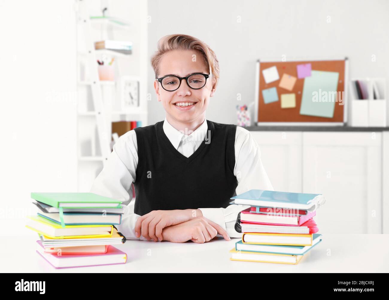 Pupil with pile of books sitting at desk in a classroom Stock Photo - Alamy