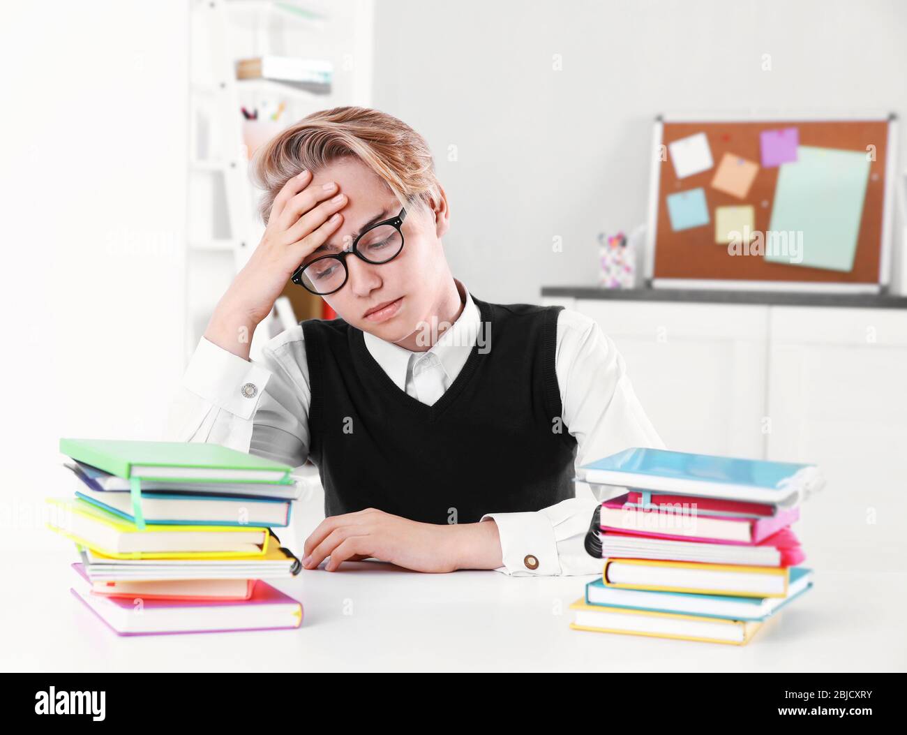 Pupil with pile of books sitting at desk in a classroom Stock Photo - Alamy