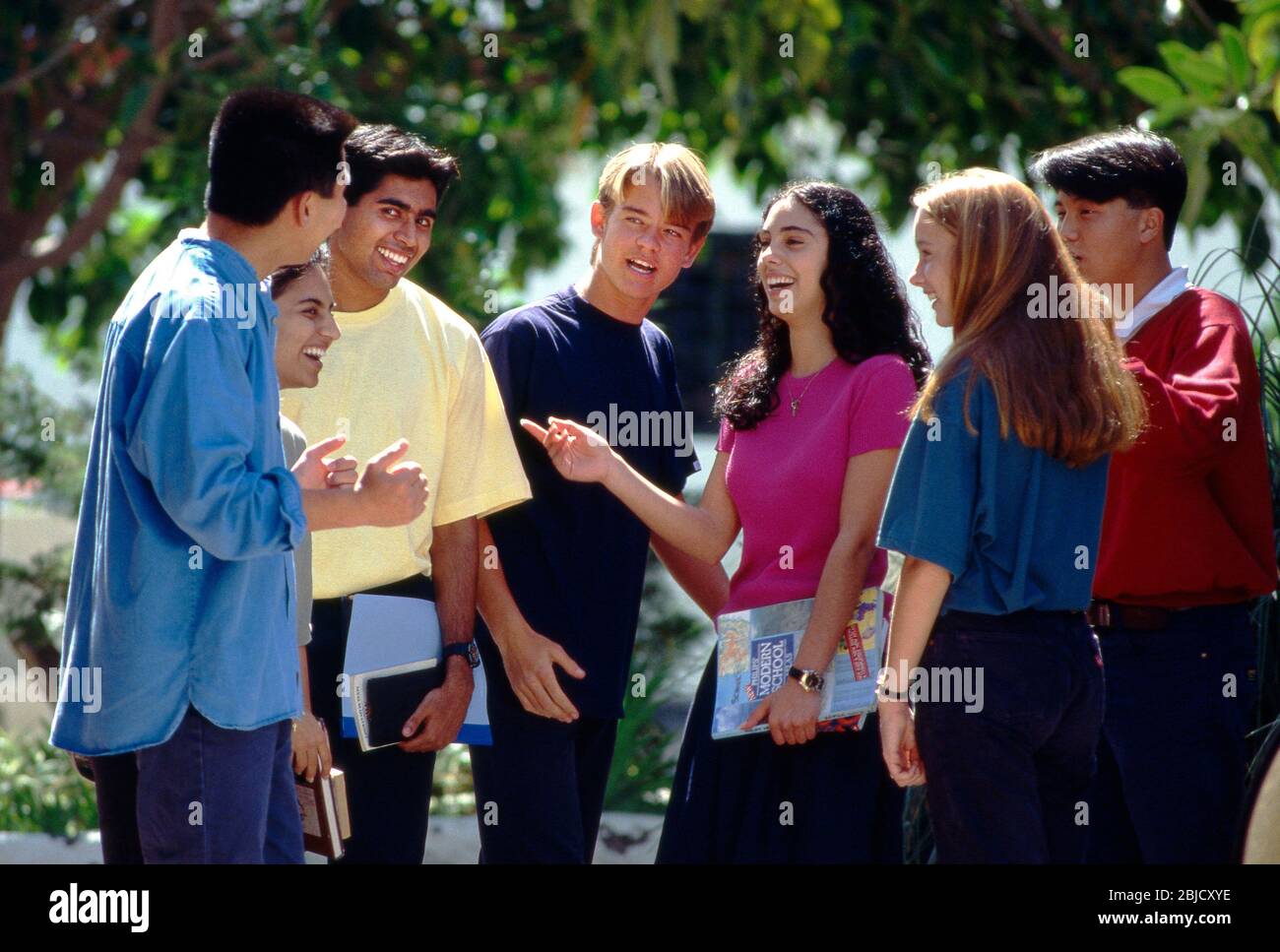 School students multicultural group of 7 happy attractive teenage senior school college high school multicultural students in colourful t shirts relaxing talking and interacting outside in a sunny school college campus environment Stock Photo