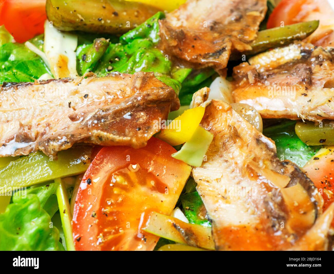 Dressed salad with tinned pilchards lettuce tomatoes yellow peppers sliced gherkins and onions Stock Photo