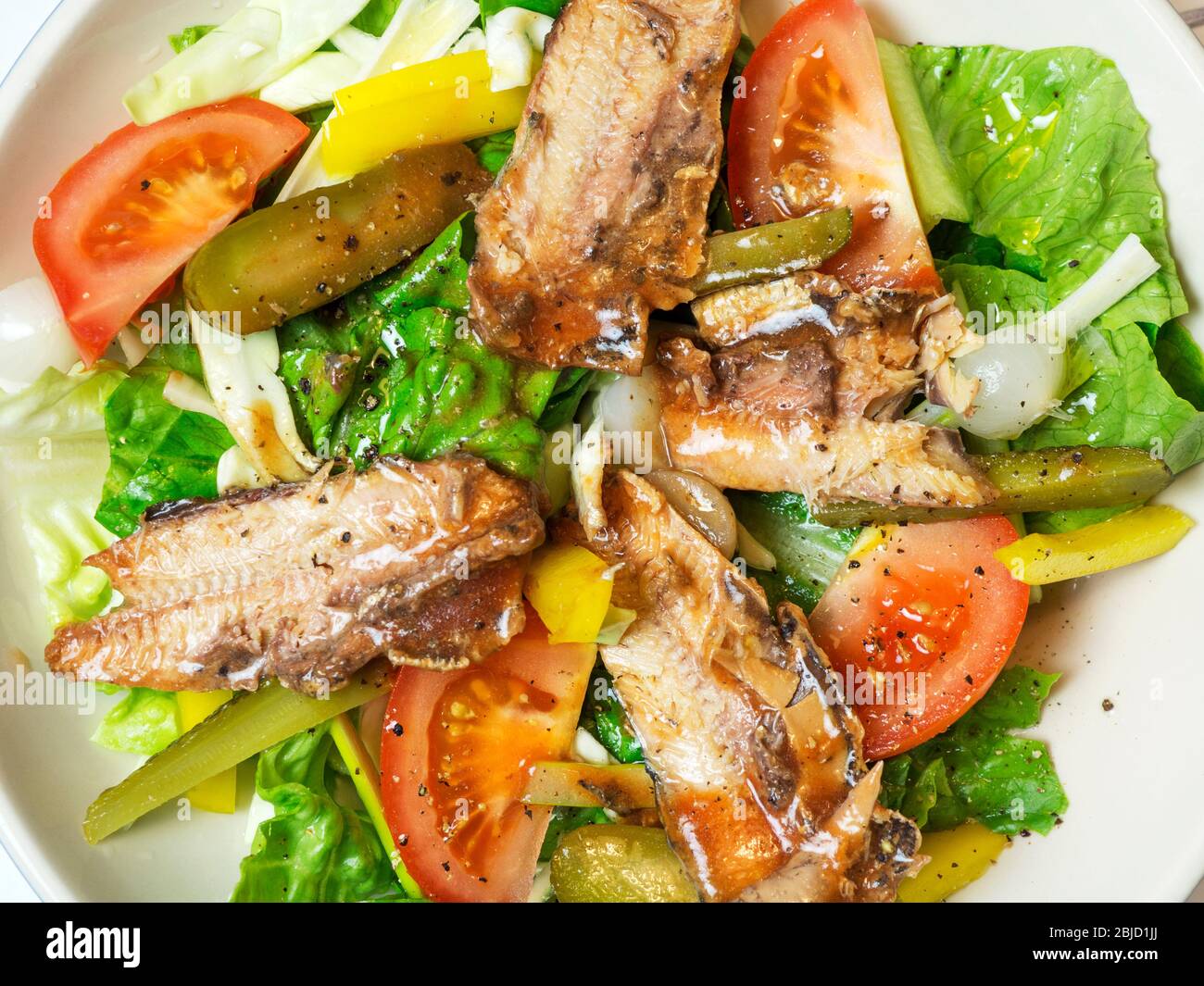 Bowl of dressed salad with tinned pilchards lettuce tomatoes yellow peppers sliced gherkins and onions Stock Photo