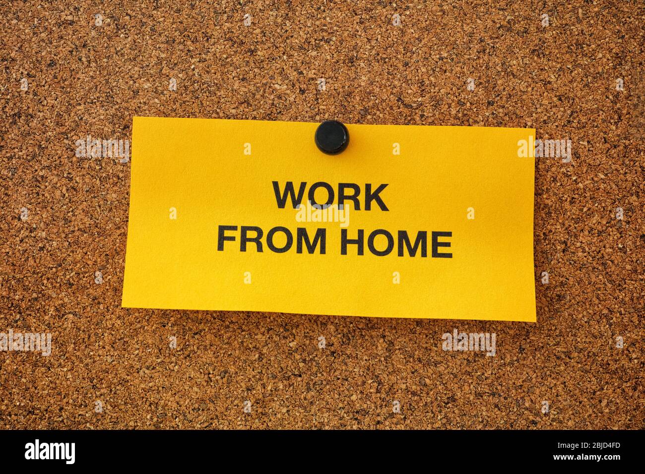 Work From Home written on a yellow piece of paper that is on a bulletin board. Remote work concept. Close up. Stock Photo