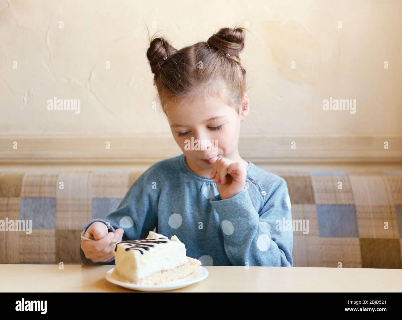 Cute little girl eating tasty cake in kitchen Stock Photo