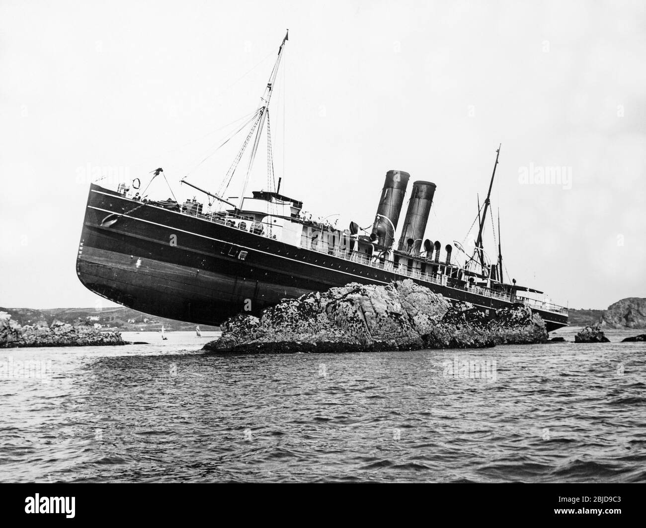 Vintage early twentieth century black and white photograph showing a steam powered cruise ship which has run aground on some rocks. The ship has two funnels, but has no name. Stock Photo
