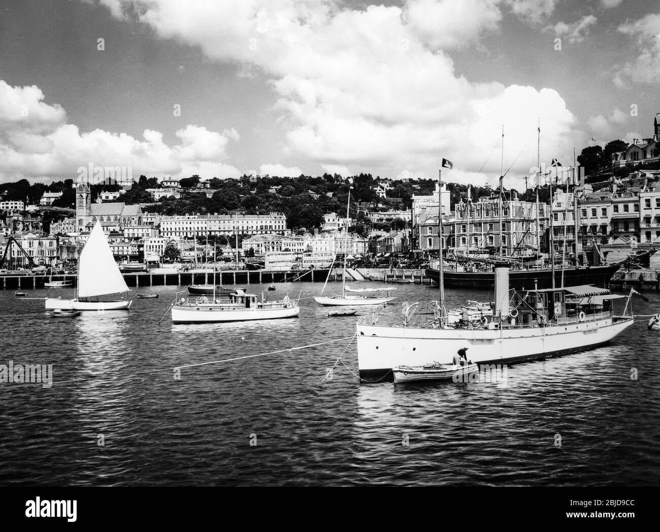 Early mid twentieth century vintage black and white photograph showing Torquay Harbour on the South Coast of England. Photo shows various boats and ships in harbour. Also visible are the White House Hotel, Norfolk Hotel, St. James Hotel, and Regina Hotel. Stock Photo