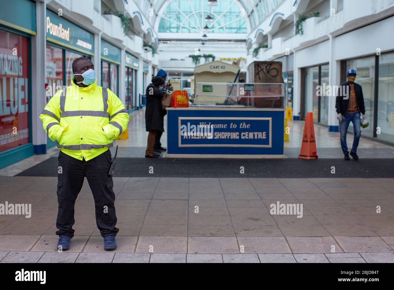 Peckham, UK. 29th April, 2020. Life in South London during the Coronavirus lockdown. A security guard wearing a protective face mask and high visibility jacket stands outside Aylesham Shopping Centre in Peckham. ( Credit: Sam Mellish/Alamy Live News ) Stock Photo