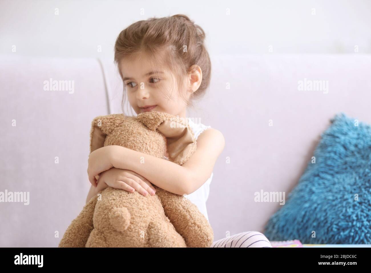 Funny little girl with cuddly toy sitting on sofa at home Stock Photo ...