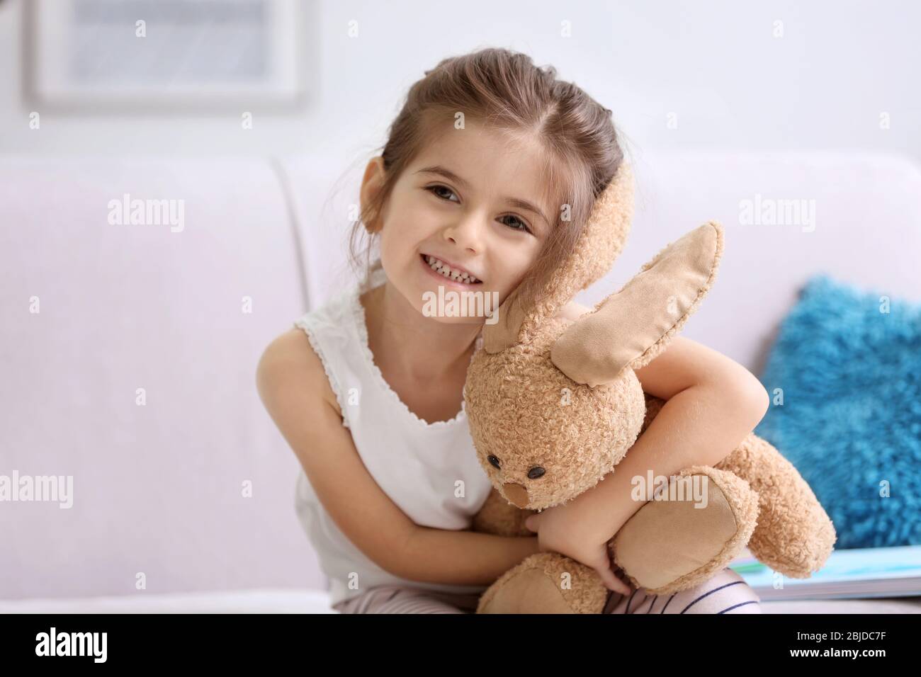 Funny little girl with cuddly toy sitting on sofa at home Stock Photo ...