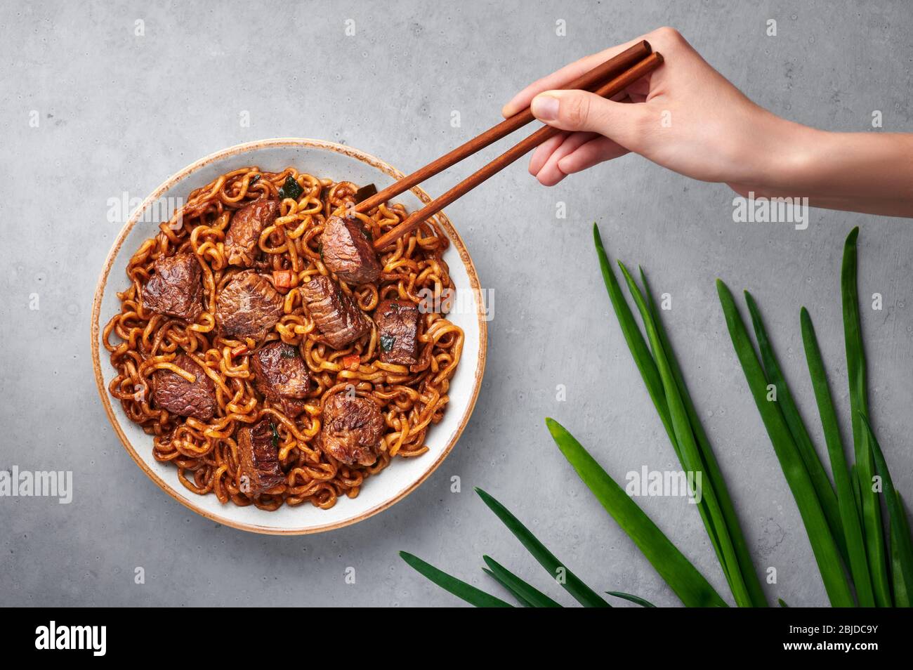 Ram-Don or Chapaguri noodles with beef steak in white bowl on grey concrete backdrop. Jjapaguri is a popular south korean dish with ramen and udon noo Stock Photo