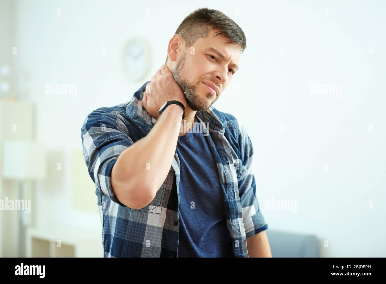 Handsome young man suffering from neck pain at home Stock Photo - Alamy
