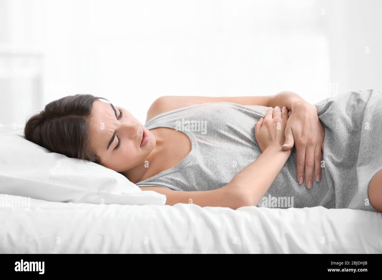 Young woman suffering from abdominal pain while lying on bed at home