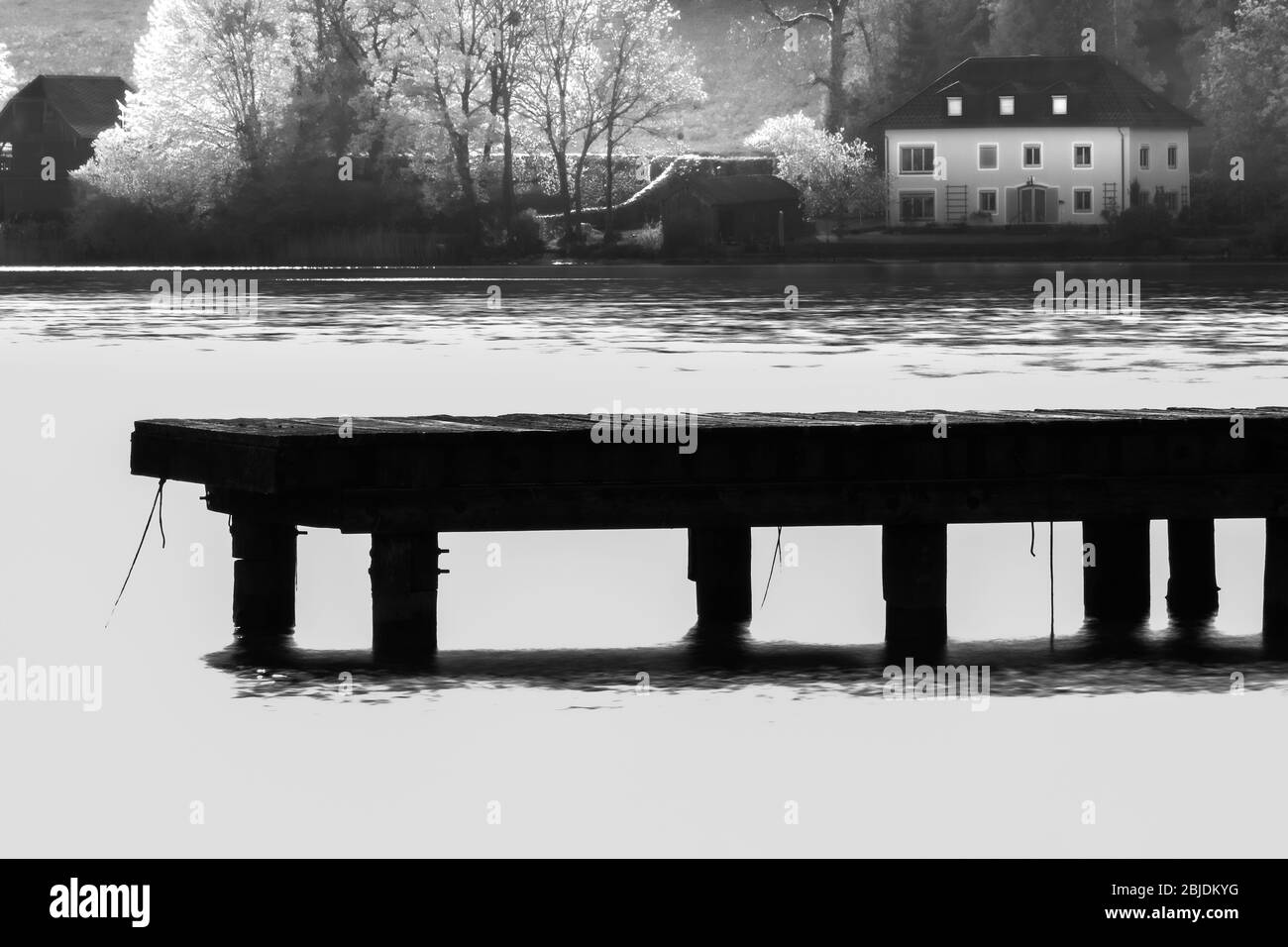 A dock extends out into a lake in Black and white Stock Photo