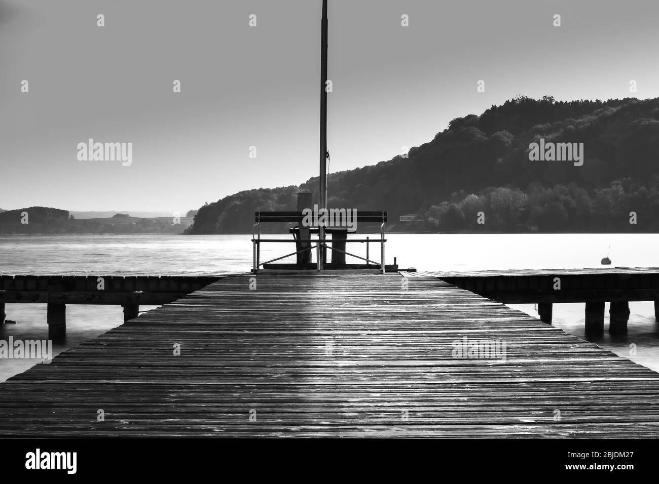 A dock extends out into a lake in Black and white Stock Photo