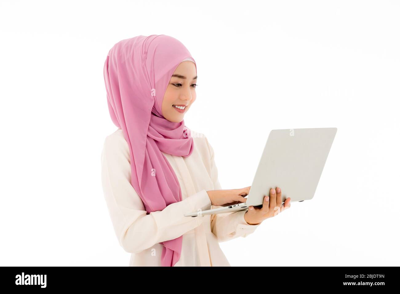 A beautiful young Asian Muslim woman in hijab is using a laptop with a ...