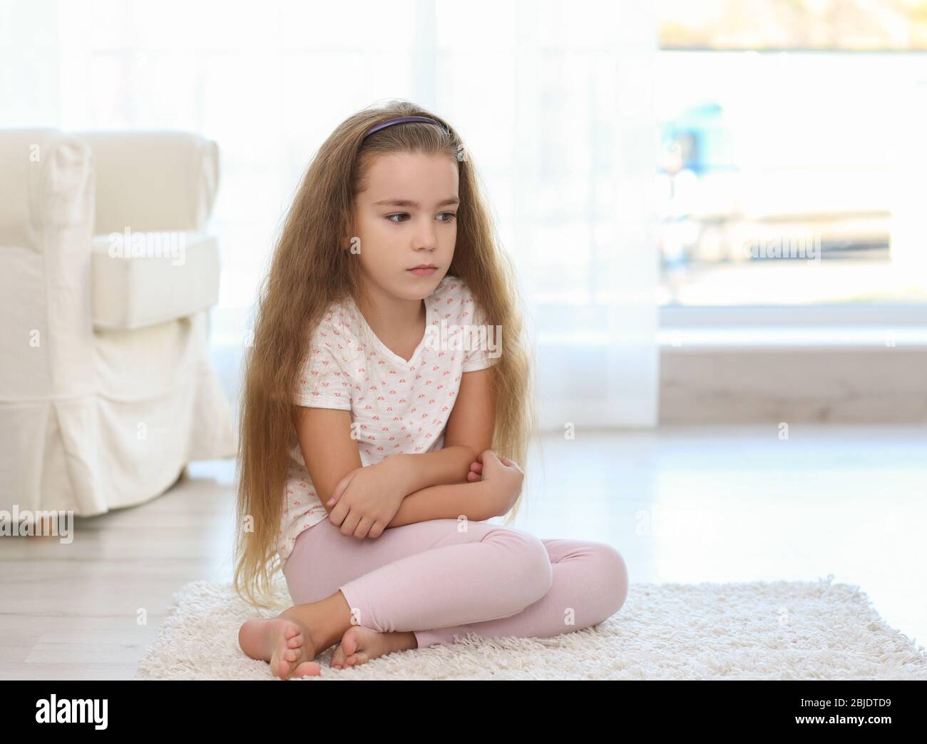 Sad little girl sitting on floor in room Stock Photo - Alamy