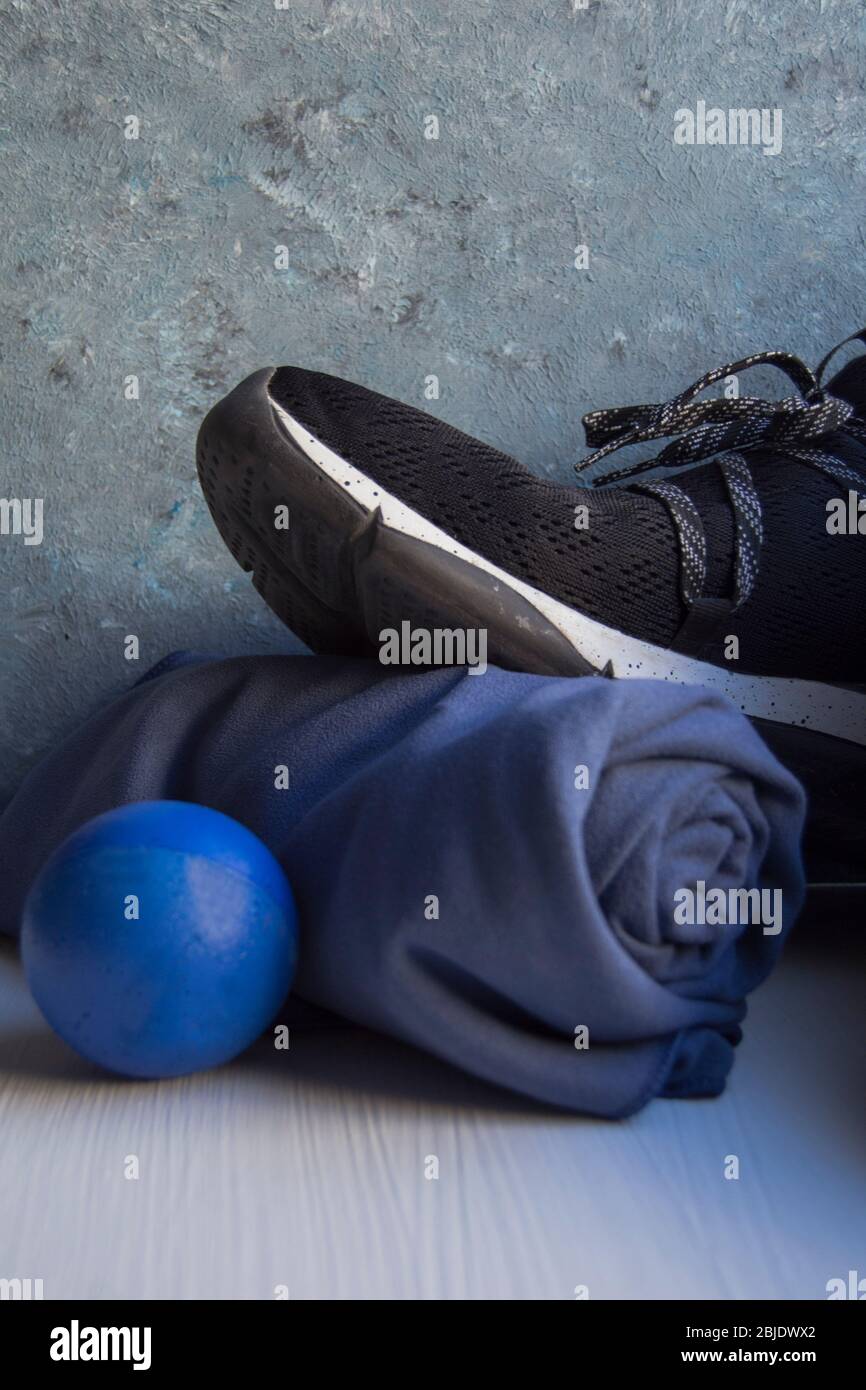 Black sneaker with white details and holes, a blue rolled towel and a blue foam rubber ball on a white base and a background in blue and gray tones. Stock Photo