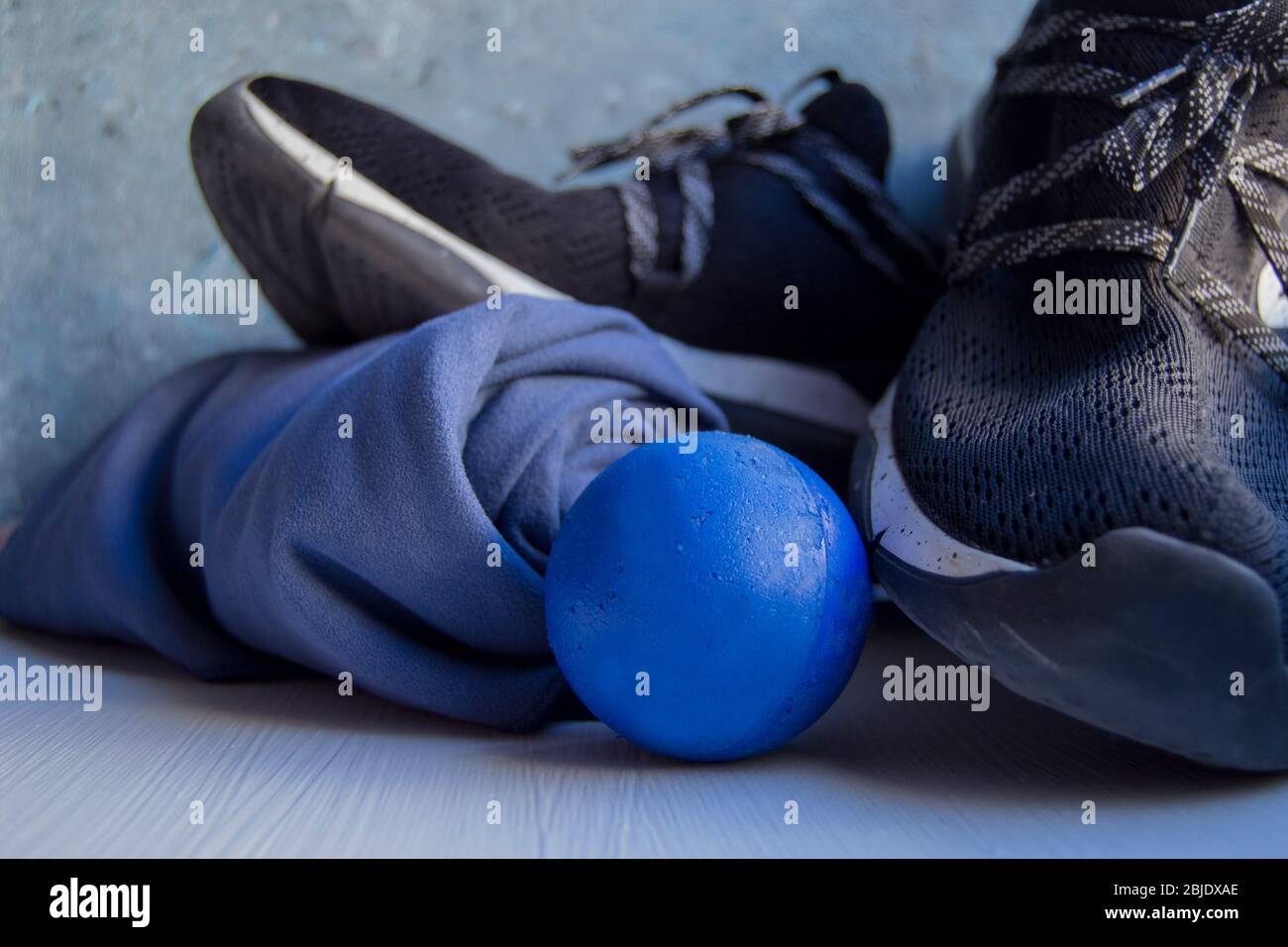 Black sneaker with white details and holes, a blue rolled towel and a blue foam rubber ball on a white base and a background in blue and gray tones. Stock Photo