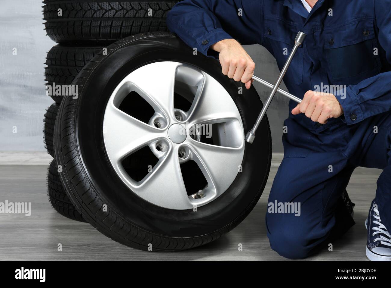 Young mechanic in uniform with spanner and wheels, on gray background