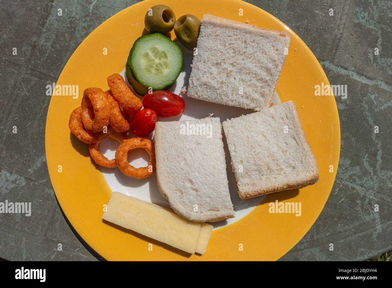 A plate of food comprising of sandwiches and salad vegetables on an old garden table. Stock Photo