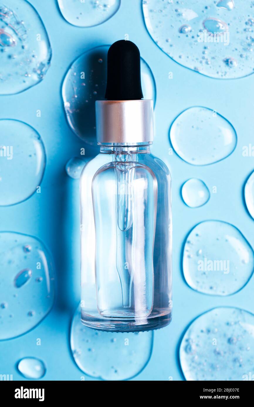Bottle of cosmetic liquid transparent gel with bubbles on blue background. Flat lay style. Stock Photo