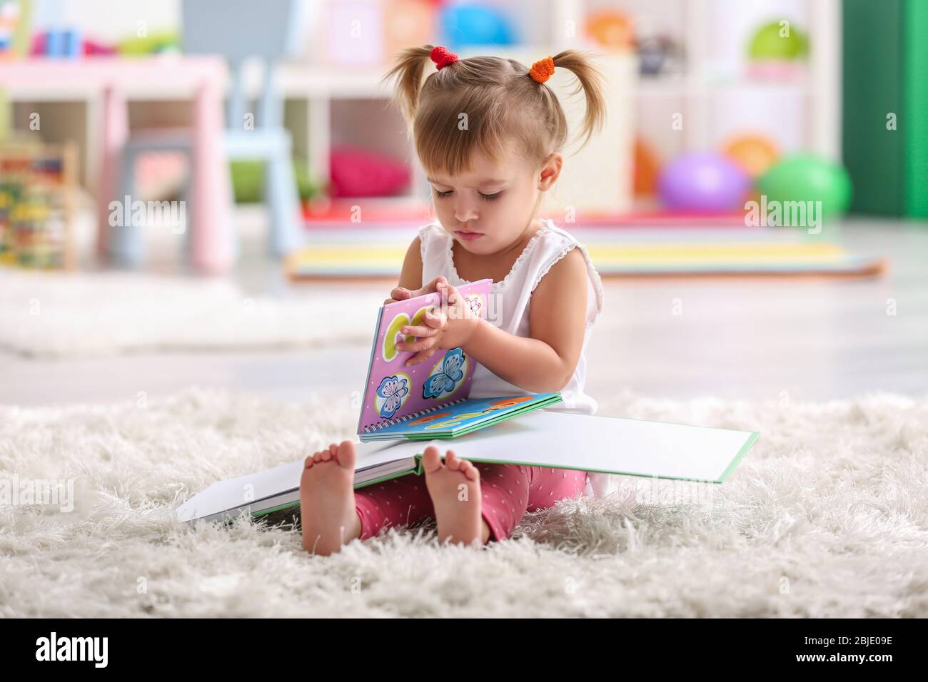 Cute little girl sitting on carpet with books Stock Photo - Alamy