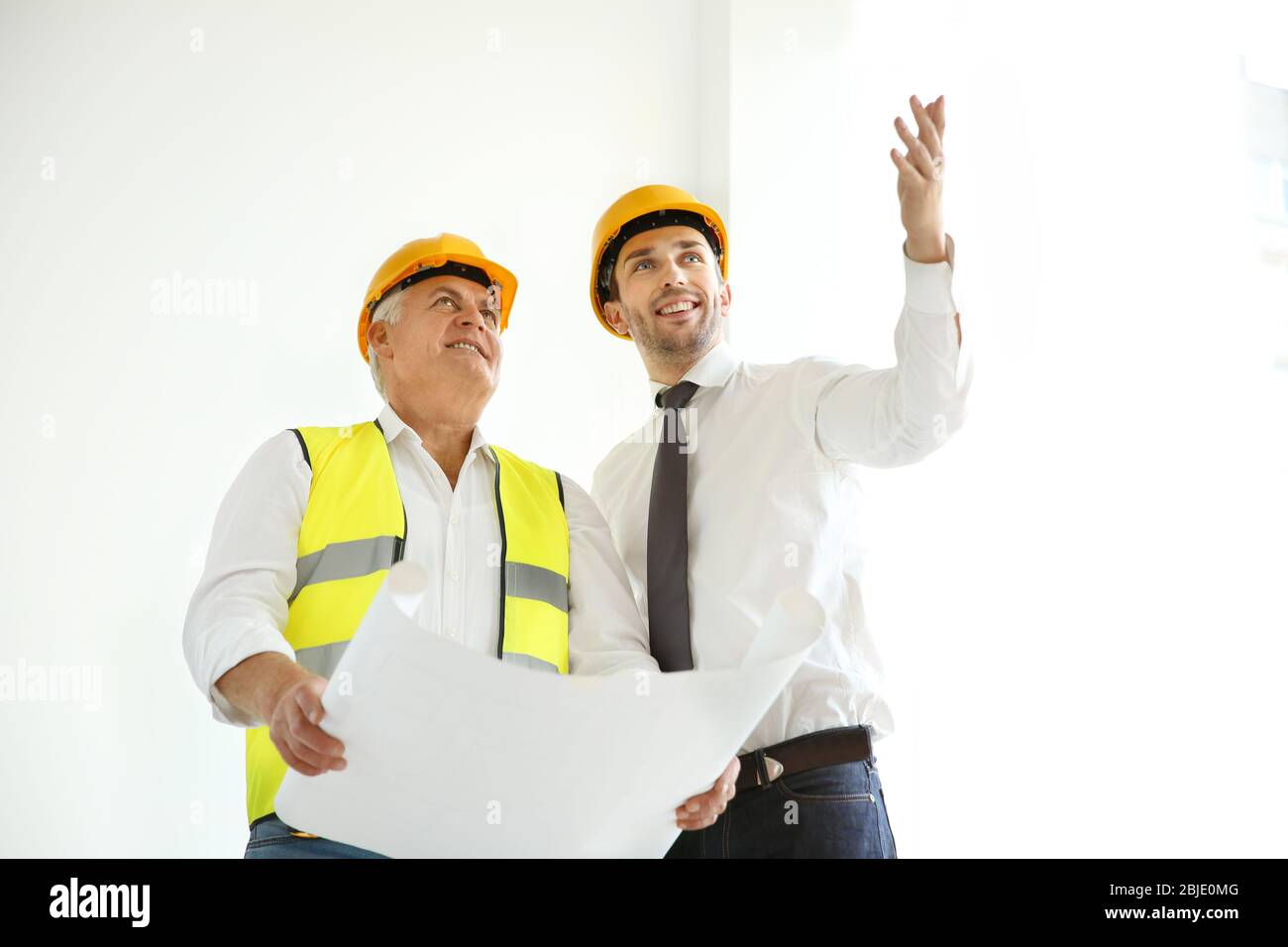 Handsome engineer and worker discussing plan of works while standing inside new building Stock Photo