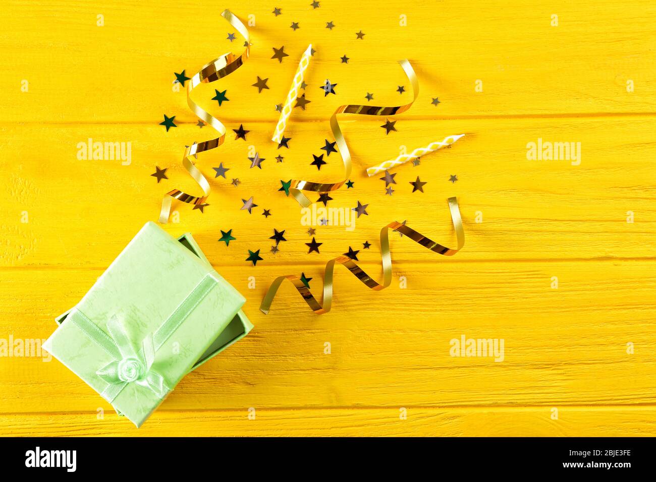 Bright confetti and gift box on wooden yellow background Stock Photo