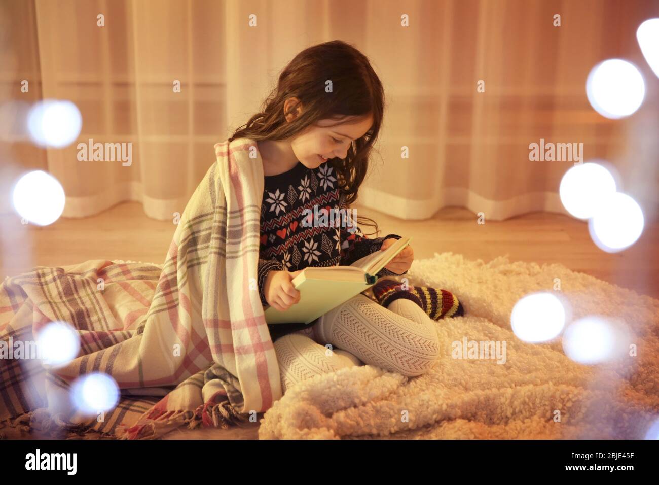 Cute little girl reading book while sitting on floor at home Stock ...