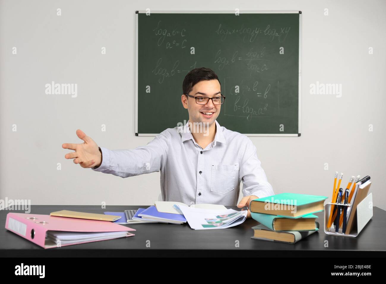 Handsome young teacher sitting at table in classroom Stock Photo